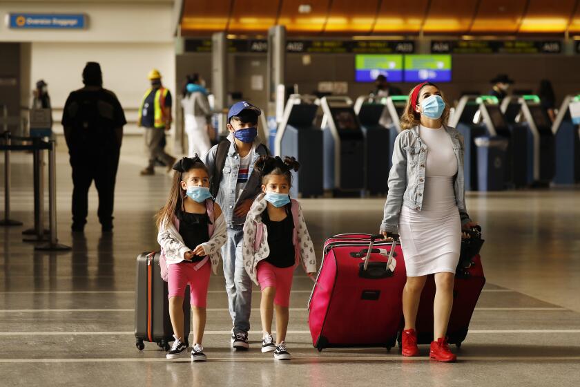 LOS ANGELES, CA - MAY 11: Yadira Barajas walks with her children Owen Vargas, 11, and 6-year-old twins Madison and Madelyn Contreras, as they prepare for a flight to Mexico at Tom Bradley International Terminal at Los Angeles International Airport (LAX) which is now requiring travelers to wear face covering to help keep fellow passengers and crew safe by limiting the spread of the coronavirus Covid-19. The new requirements for wearing face masks in Los Angels began Monday at LAX and on local public transit. LAX on Monday, May 11, 2020 in Los Angeles, CA. (Al Seib / Los Angeles Times)