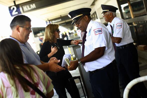 Henry Watts, a skycap at Los Angeles International Airport for 20 years, accepts payment and a tip from Phil Kyko of Bloomfield Hills, Mich., after checking in the family's bags. The fortunes of skycaps at LAX and elsewhere are fading rapidly due to an unprecedented economic downturn in the airline industry that has cut their earnings and reduced the hours of some workers.