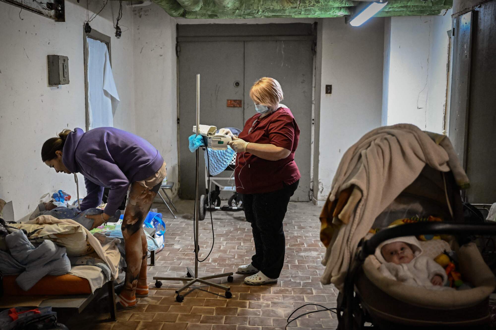 A nurse checks a baby in a basement while another person stands nearby