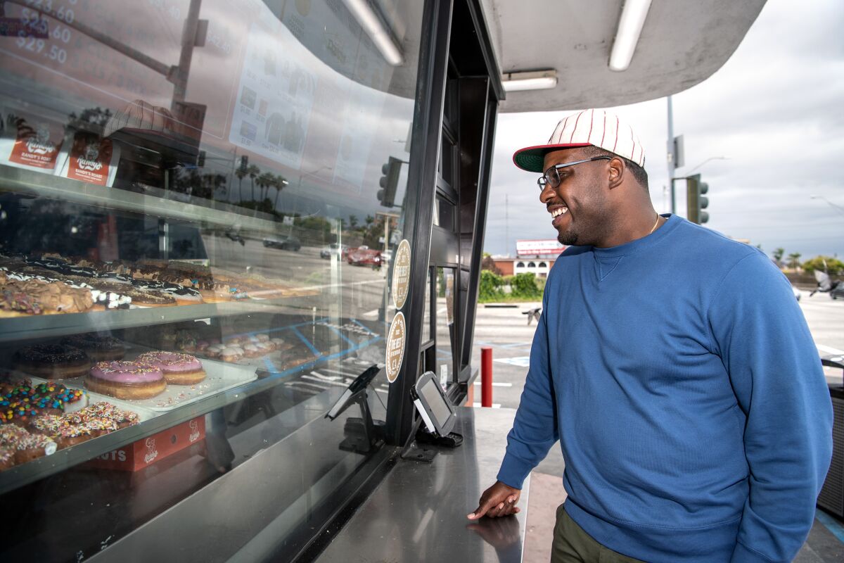 A man smiles as he stands outside of a donut shop