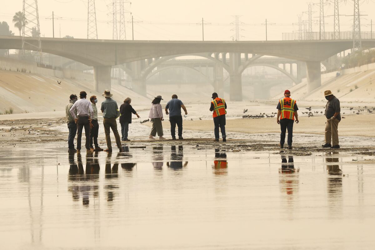 People stand in the shallow trickle of water in the concrete LA River channel