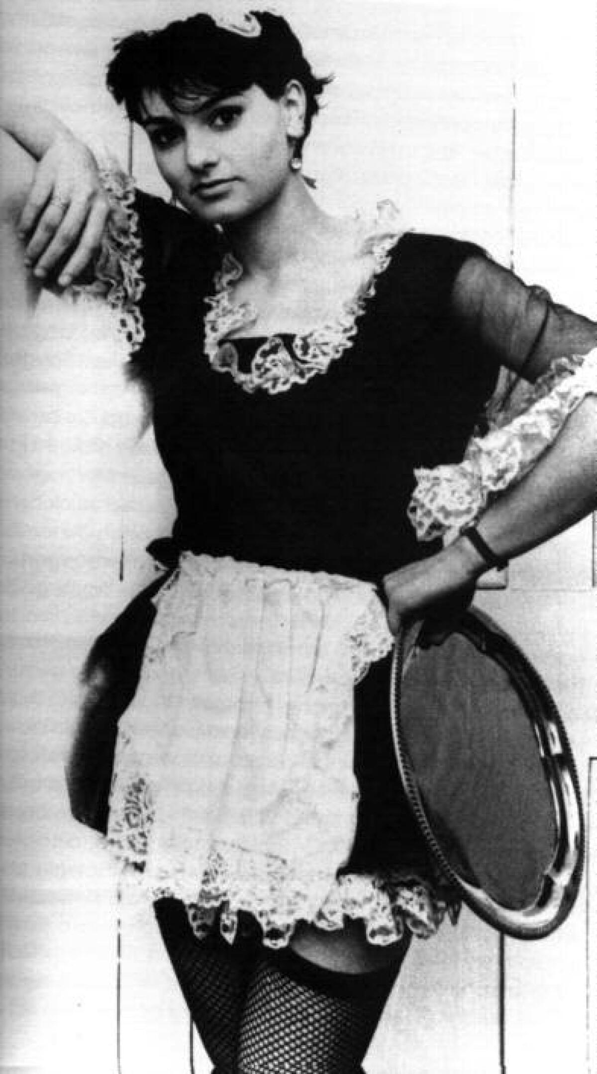 Teenage Sinéad O'Connor dressed in a short waitress dress and fishnet stockings, holding a tray.