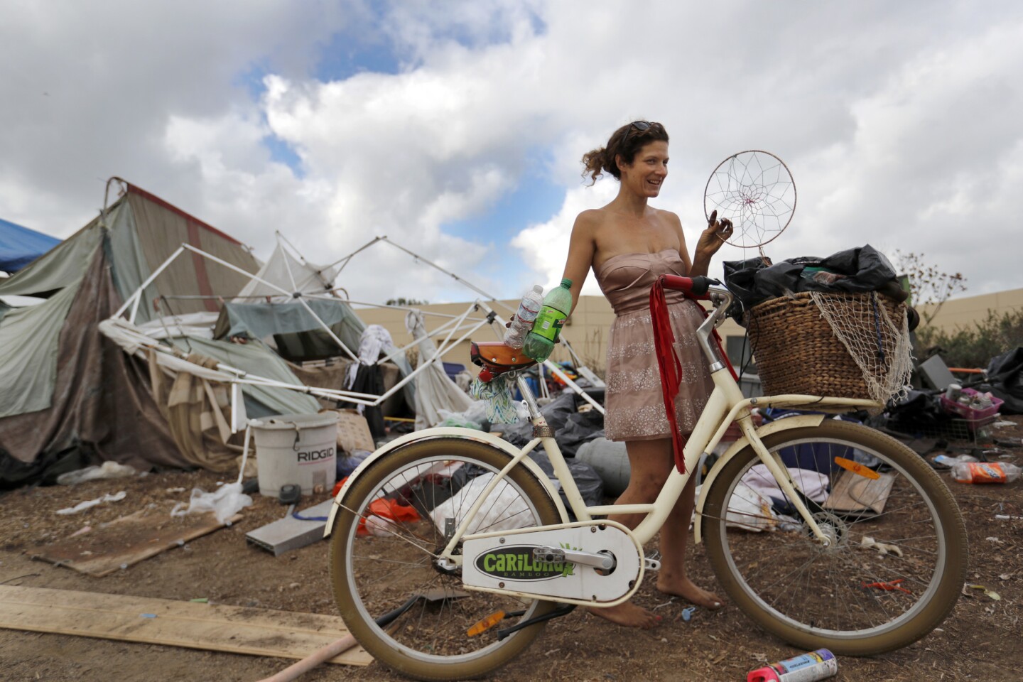Morgan Gallerito wears a glamorous dress and holds a homemade dream catcher while being evicted with her belongings from a large homeless encampment along the Santa Ana River trail Friday.