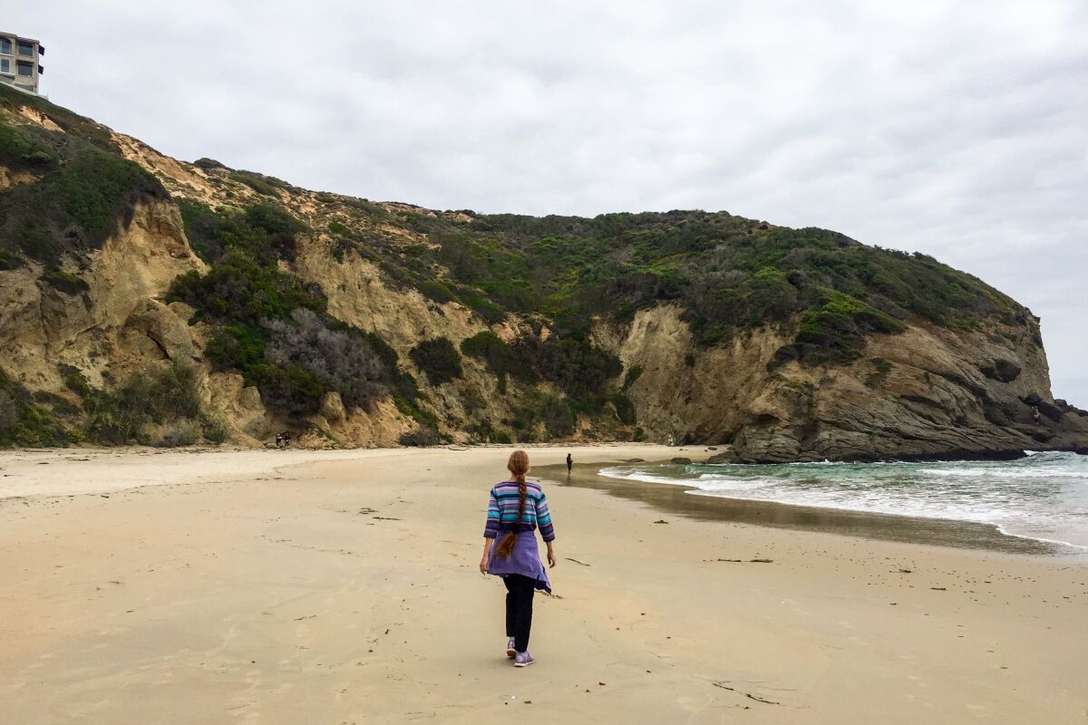 A woman walks on the beach toward ocean-facing rocks  