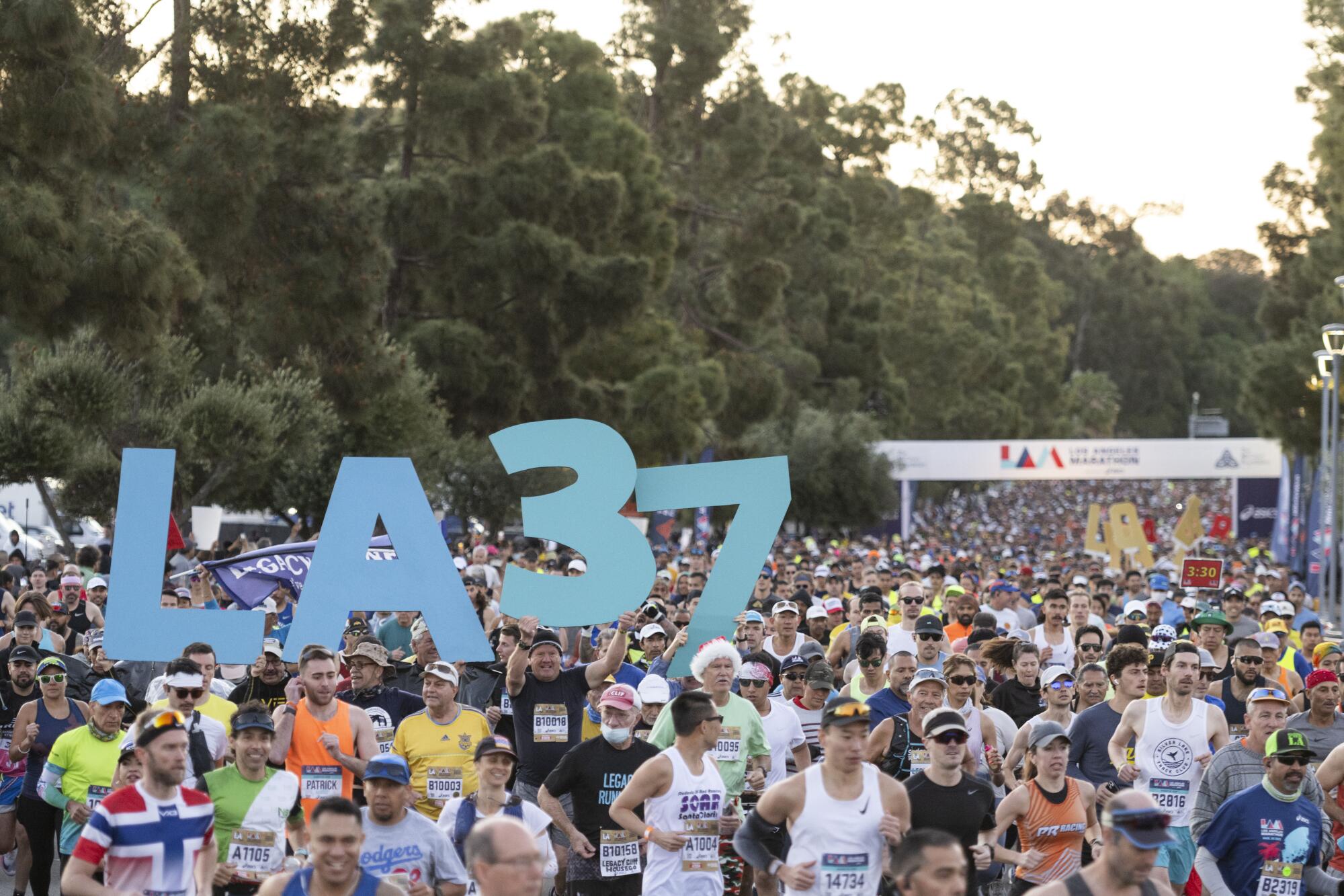Signs reading "LA 37" are held above a crowd of runners