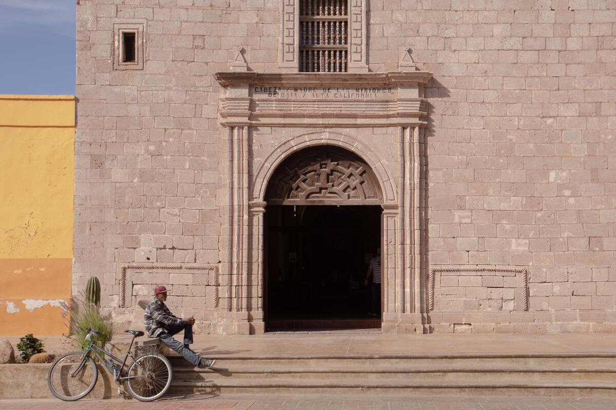 A man with a bicycle sitting in front of the entrance to a church.