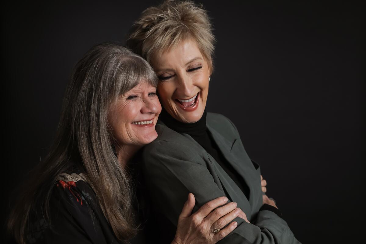 Two women laugh and hold each other for a portrait.