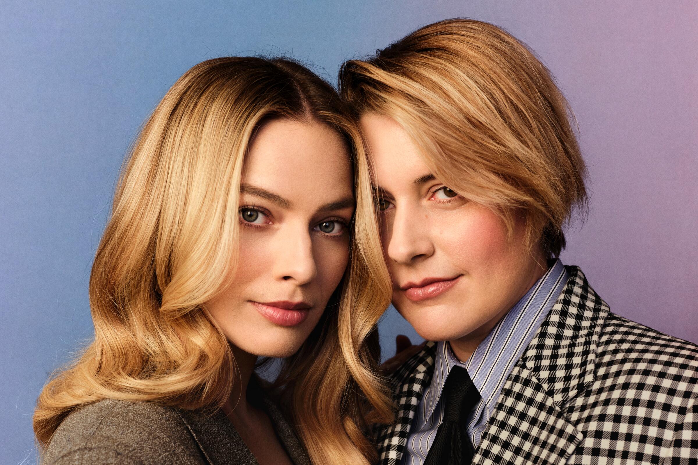 Margot Robbie and Greta Gerwig stand close together, heads touching.