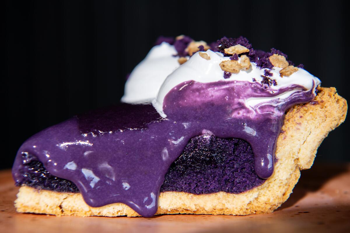 A slice of pie with dark purple filling, creamy purple spilling over the sides, whipped cream and nuts