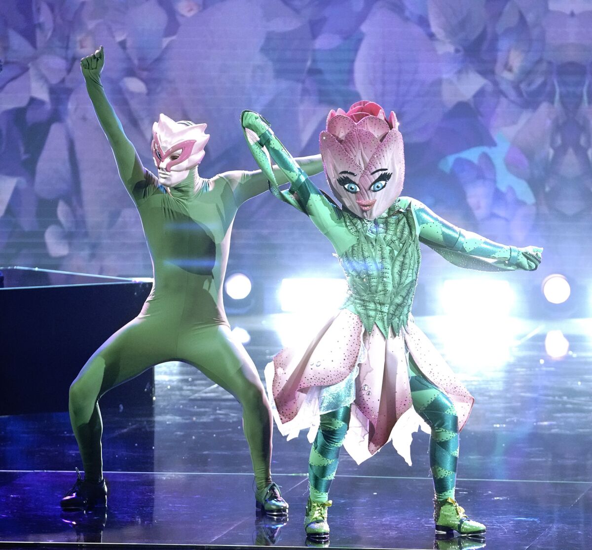 Two people in green leotards with tulip headdresses dance on stage.