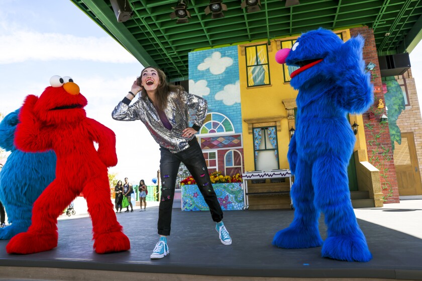 A woman dances with Sesame Street characters on stage at Sesame Place