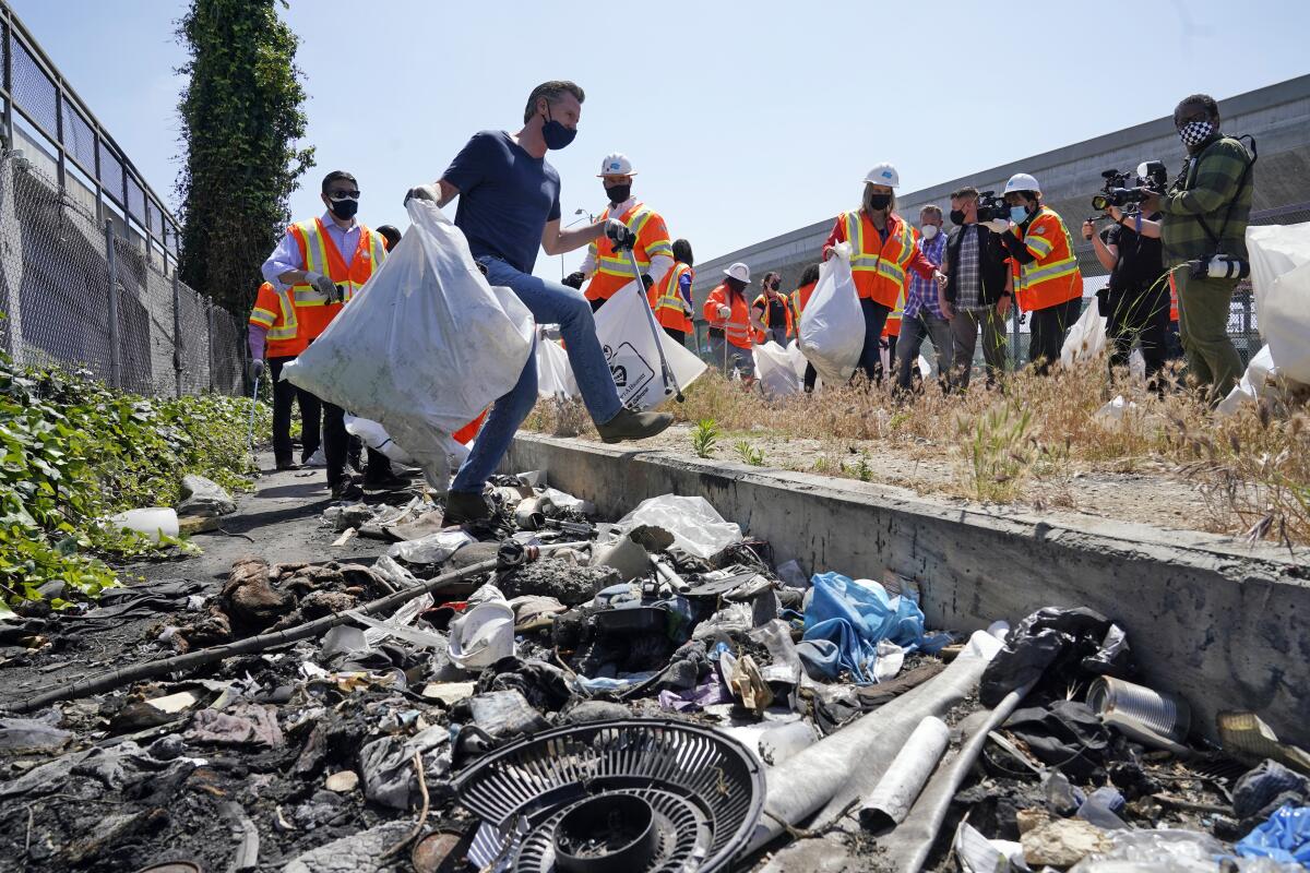 Gov. Gavin Newsom carries trash bags surrounded by work crew members.