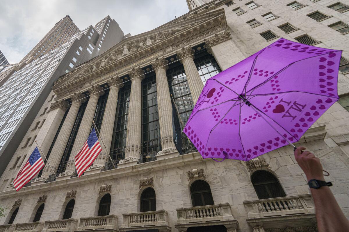 A tour group leader holding an umbrella passes the front of the New York Stock Exchange. 