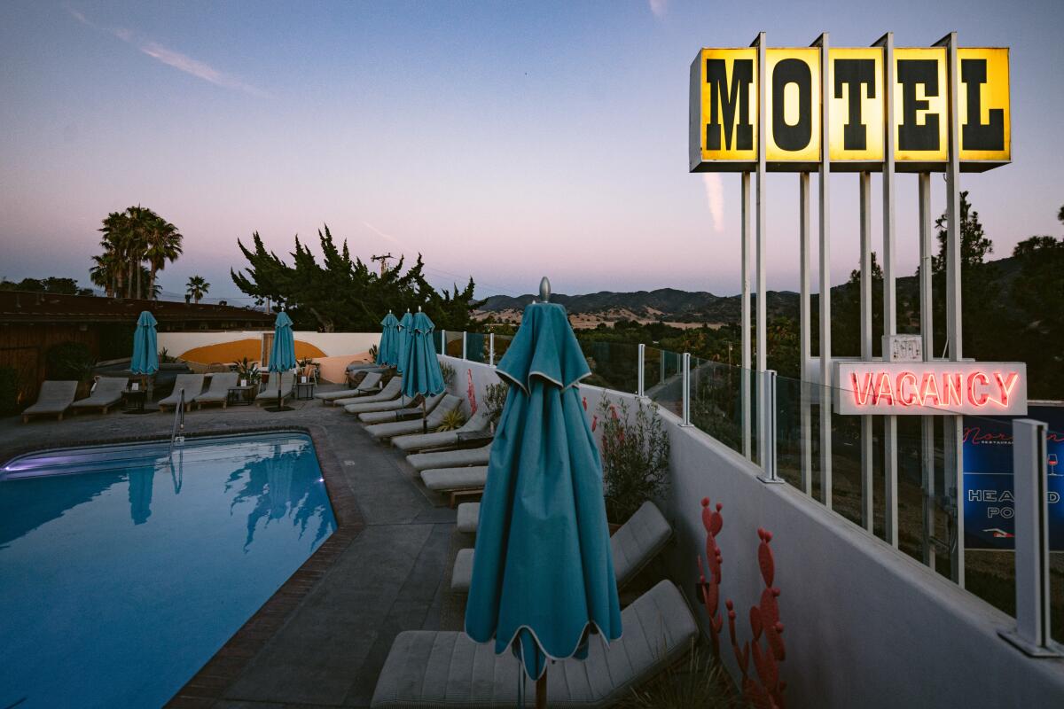 A yellow motel sign looming above an empty pool at dusk.