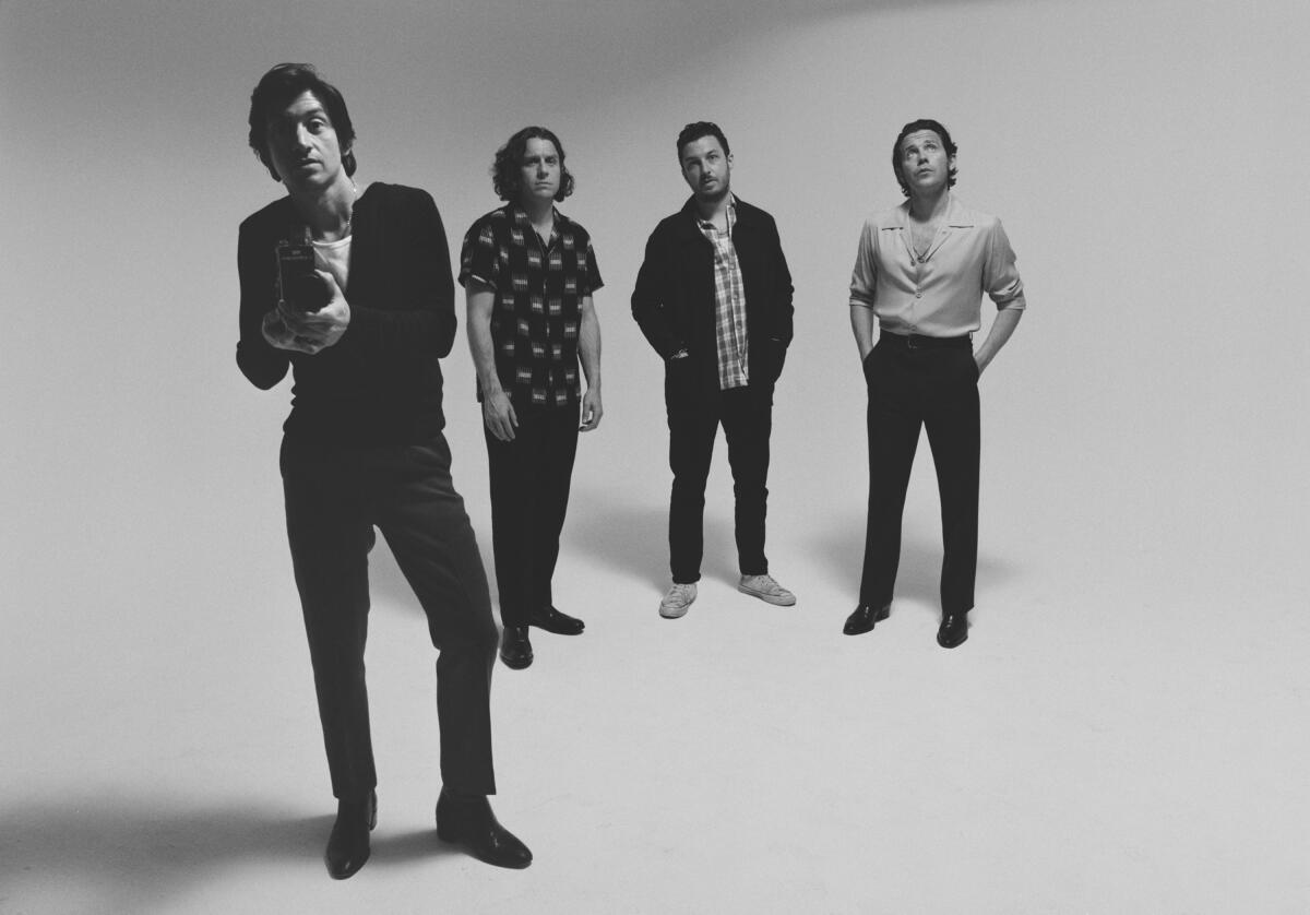 Four guys in a band stand together, with one holding a camera, in a black-and-white photo