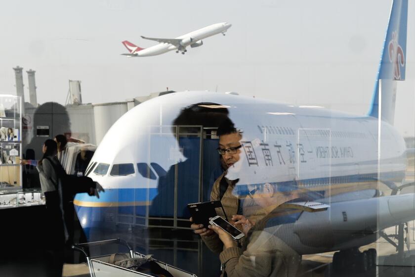FILE - Passengers walk past a couple browsing their smartphones near a China Southern Airlines, parked on the tarmac at the Beijing Capital International Airport Saturday, Nov. 19, 2016. The biggest U.S. airlines and their unions are asking the Biden administration in a letter Thursday, April 11, 2024, to stop approving more flights to the United States by Chinese airlines. (AP Photo/Andy Wong, File)