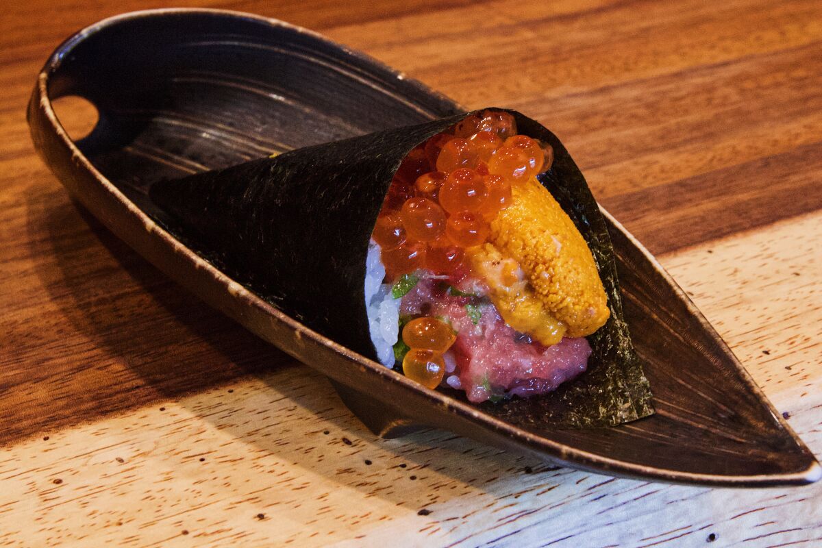 A hand roll bursting with negitoro, ikura, shiso and uni on a gold-rimmed black plate