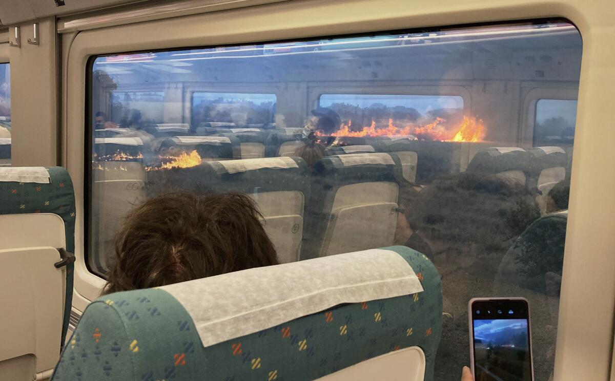 Passengers take photos at a wildfire while traveling on a train in Zamora, Spain, Monday, July 18, 2022. When Francisco Seoane's train unexpectedly stopped in Spanish countryside that was being engulfed by a wildfire, he and other passengers got a fright when they looked out at flames encroaching on both sides of the track. The Spaniard told The Associated Press it was scary to see how quickly the fire spread. Video of the unscheduled — and unnerving — stop shows about a dozen passengers in Seoane's railcar appearing alarmed as they look out of the windows Monday. (AP Photo/Francisco Seoane Perez)