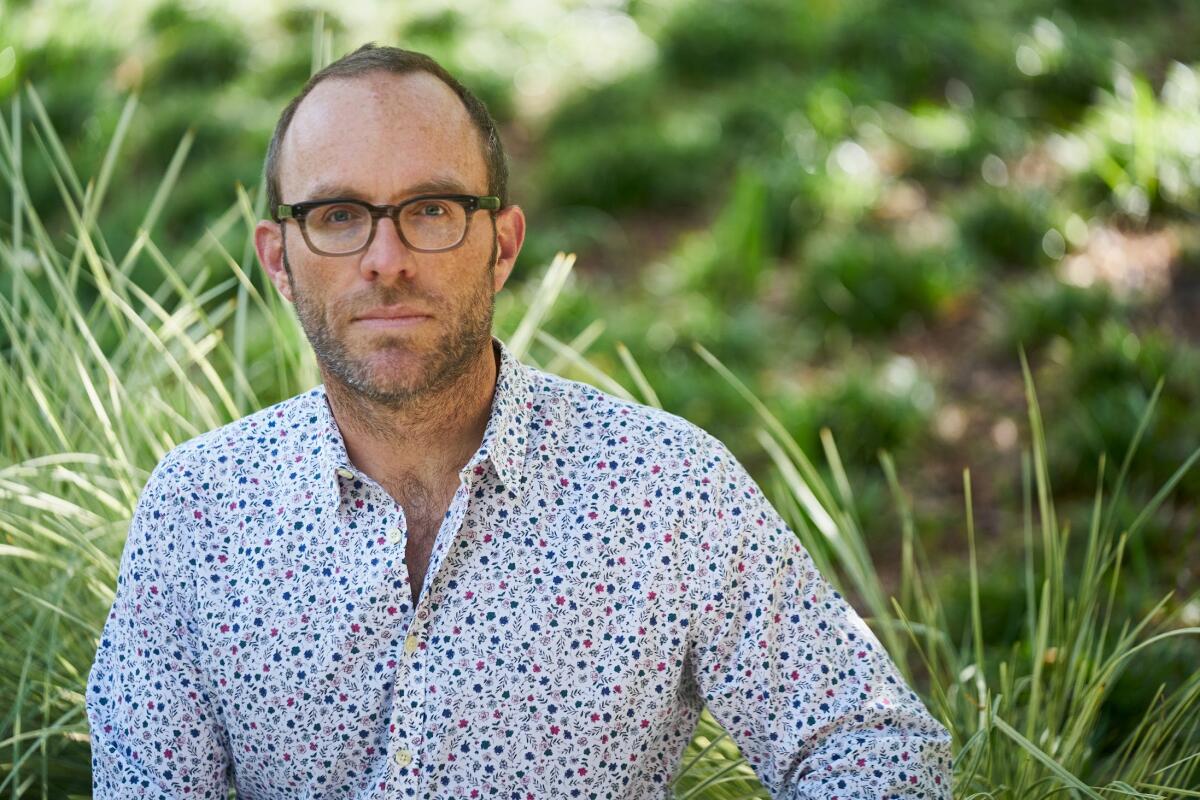 A headshot of a man outside wearing a polkadotted button-down shirt 