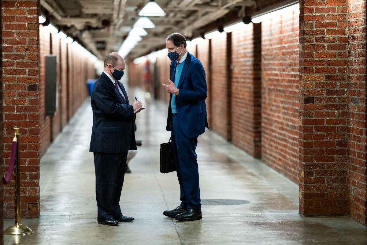Two men in suit and tie talk in a brick-lined hallway 