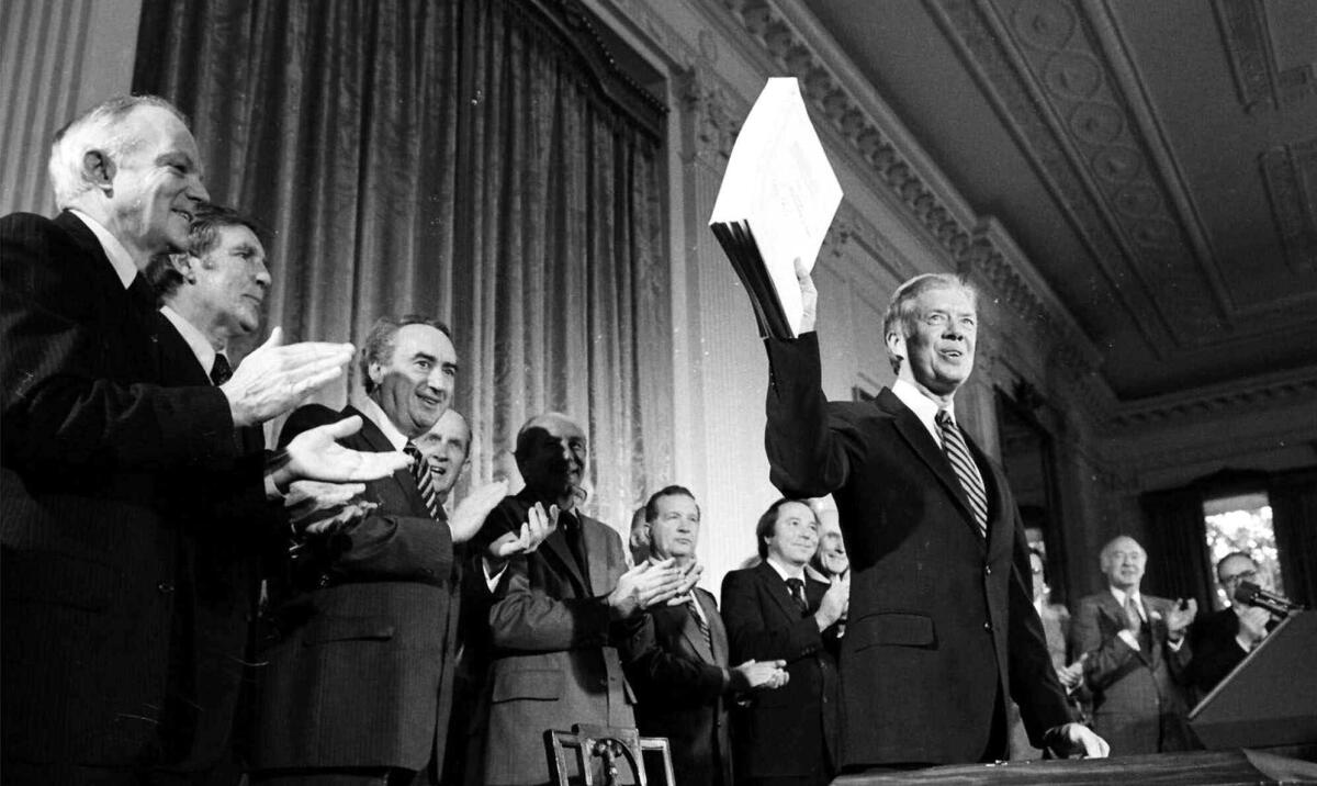 President Carter holds a stack of papers while people behind him applaud.