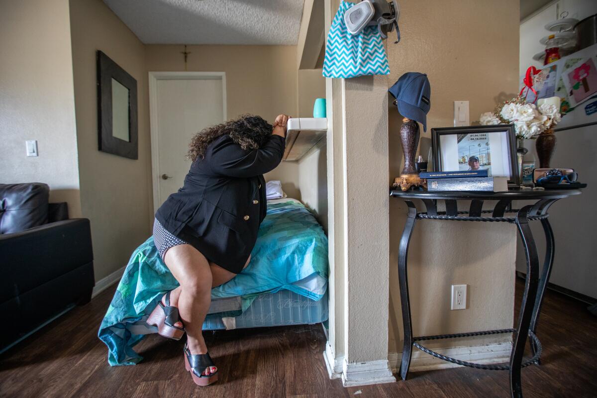 Ruth Lopez sites on the edge of her bed, resting her head in her arms, which she's resting against a shelf.