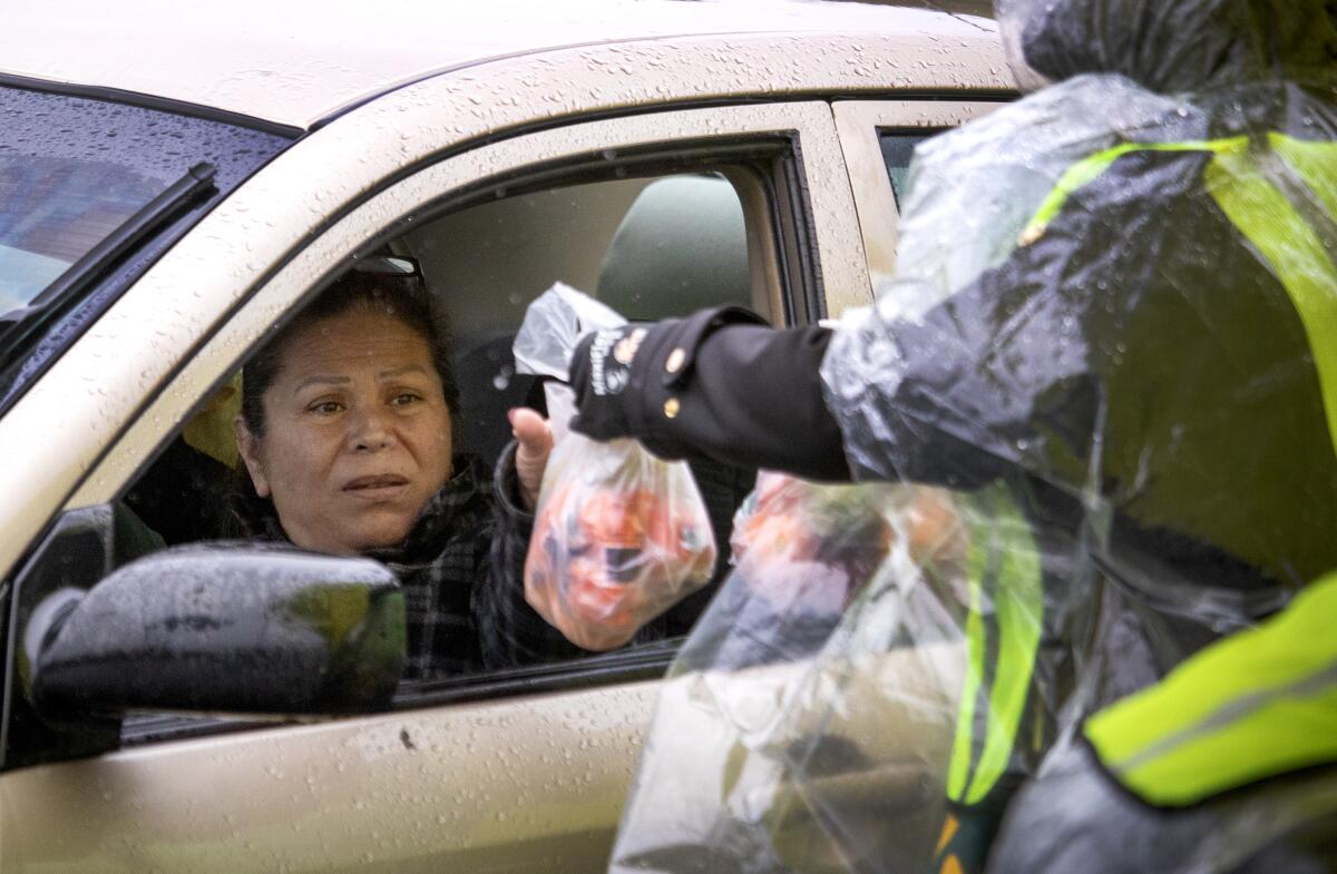 A woman reaches out of a front seat of a car for a plastic bag with food.