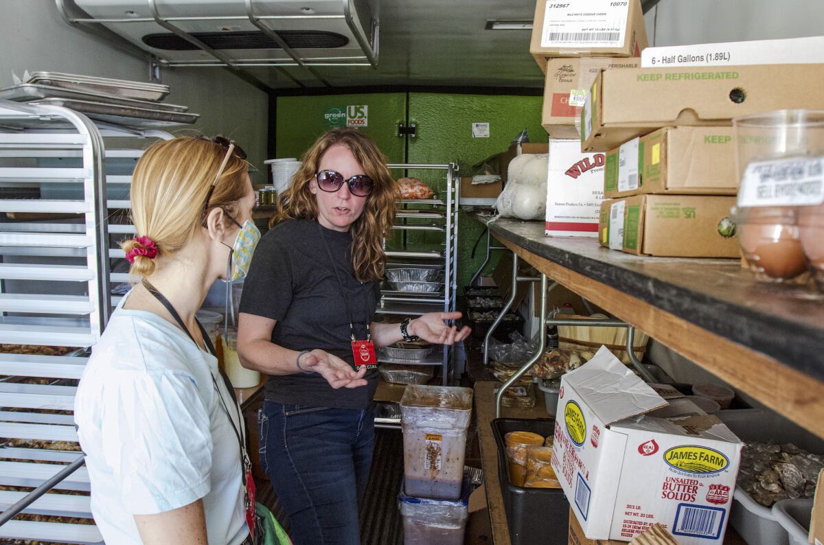 Two women stand amid shelves of eggs, butter and other unopened foods within the Players Tailgate's refrigerated truck.