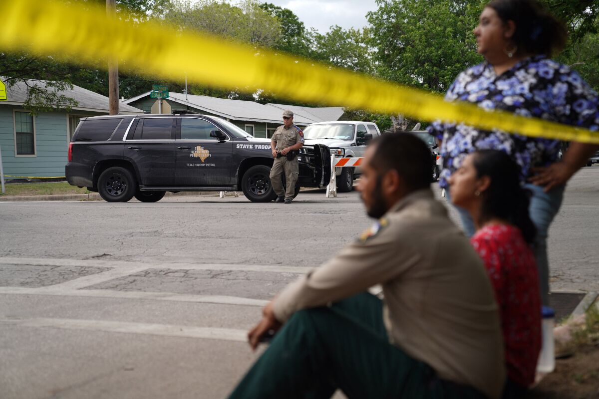 People sit on the curb outside of a school as Texas state troopers guard the area 