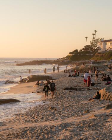 People walk along the beach around sunset at Windansea in San Diego, California. Photographed in June 2024.
