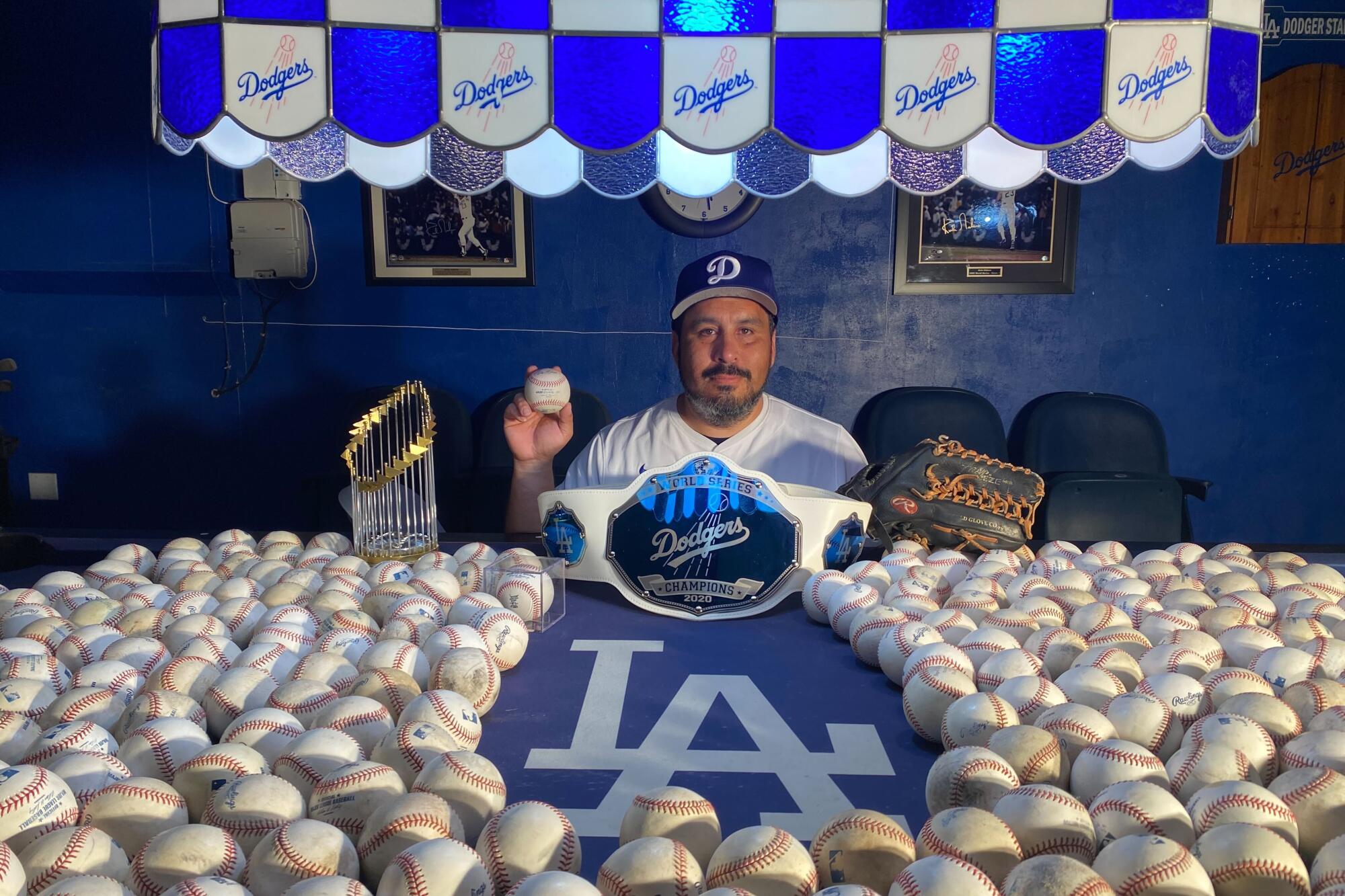 Renan Zuniga sits in his man cave surrounded by Dodgers memorabilia while holding the home run ball he caught.