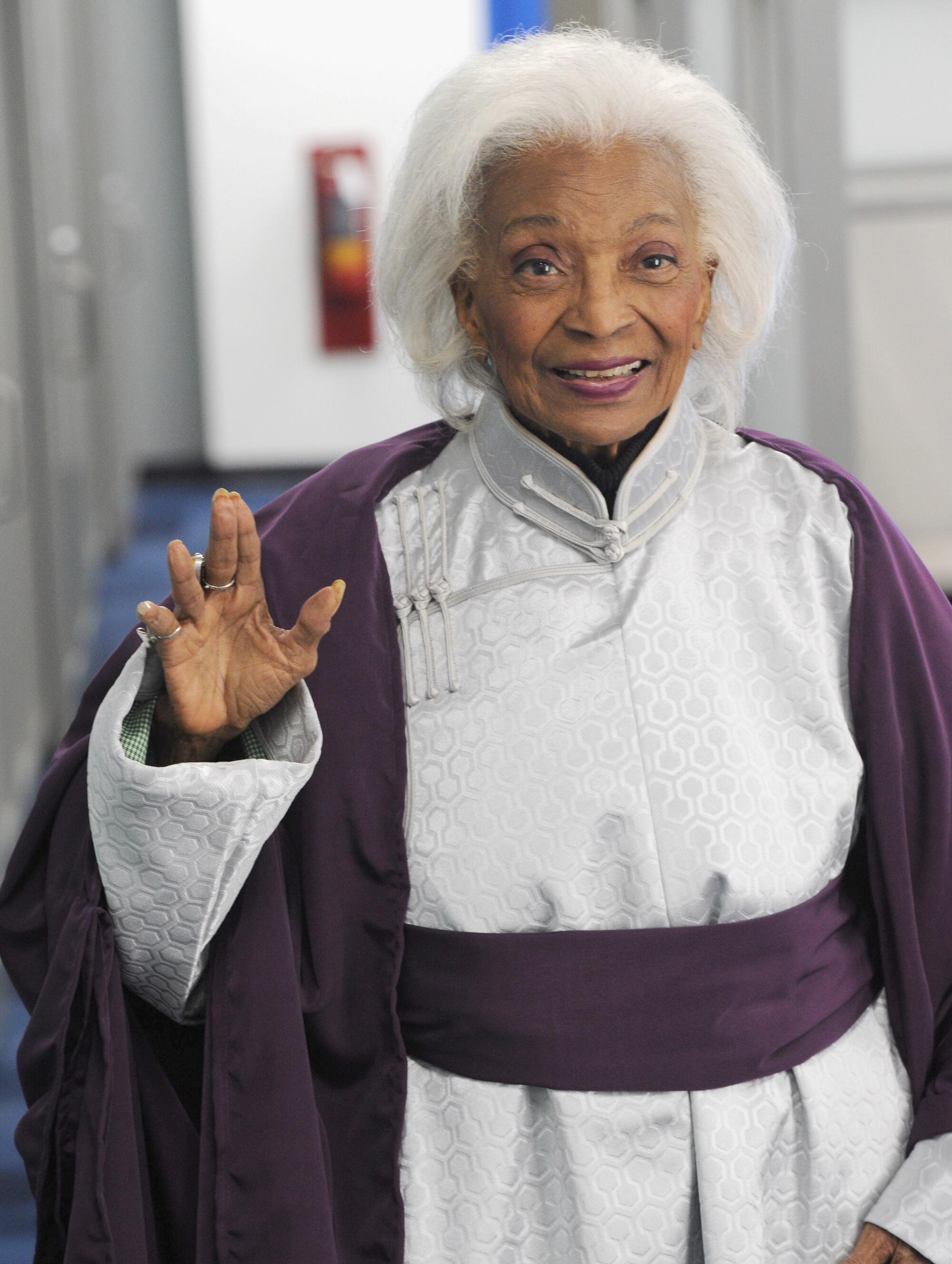 A woman with white hair smiles and spreads her fingers in a "Star Trek" symbol