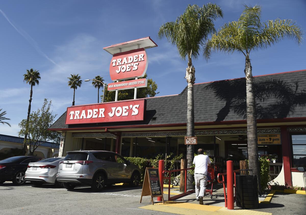A photo of a Trader Joe's, with multiple palm trees in front and a man walking with his cart into the store.