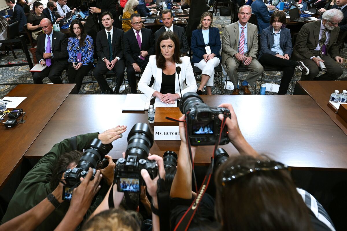 A woman sits at a table with cameras pointed at her.