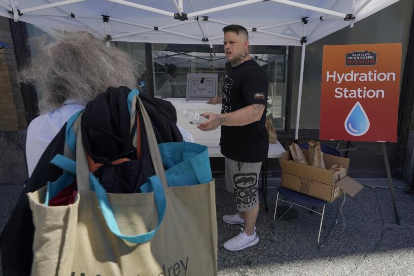 Carlos Ramos hands out bottles of water and sack lunches, Monday, June 28, 2021, as he works at a hydration station in front of the Union Gospel Mission in Seattle. Seattle and other cities broke all-time heat records over the weekend, with temperatures soaring well above 100 degrees Fahrenheit (37.8 Celsius). (AP Photo/Ted S. Warren)