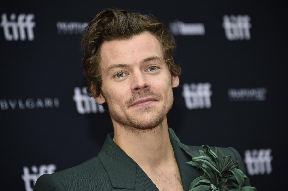 Harry Styles in front of a step-and-repeat backdrop reading "tiff" in dark green suit with leafy adornment 