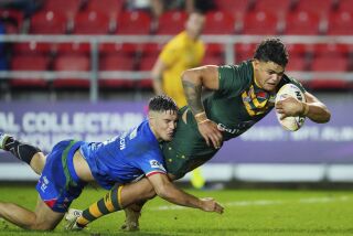 FILE - Australia's Latrell Mitchell, right, scores a try as Italy's Radean Robinson tries to defend during the Rugby League World Cup match between Australia and Italy at the Totally Wicked Stadium, St Helens, England, on Oct. 29, 2022. The National Rugby League said Friday, March 10, 2023, it is investigating the racial abuse of star South Sydney fullback Latrell Mitchell during a game on Thursday. Mitchell, who is of Indigenous descent, was verbally abused by a teenage fan wearing a Sydney Roosters jersey. The fan left at halftime of the match at a stadium in western Sydney. (AP Photo/Jon Super, File)