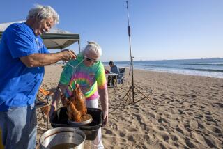 HUNTINGTON BEACH, CA - NOVEMBER 25: Chip Margelli and wife Janet Margelli of Garden Grove are deep-frying a turkey in peanut out at Bolsa Chica State Beach at on Thursday, Nov. 25, 2021 in Huntington Beach, CA. He says he has been celebrating Thanksgiving at the beach for over 15 years. (Francine Orr / Los Angeles Times)