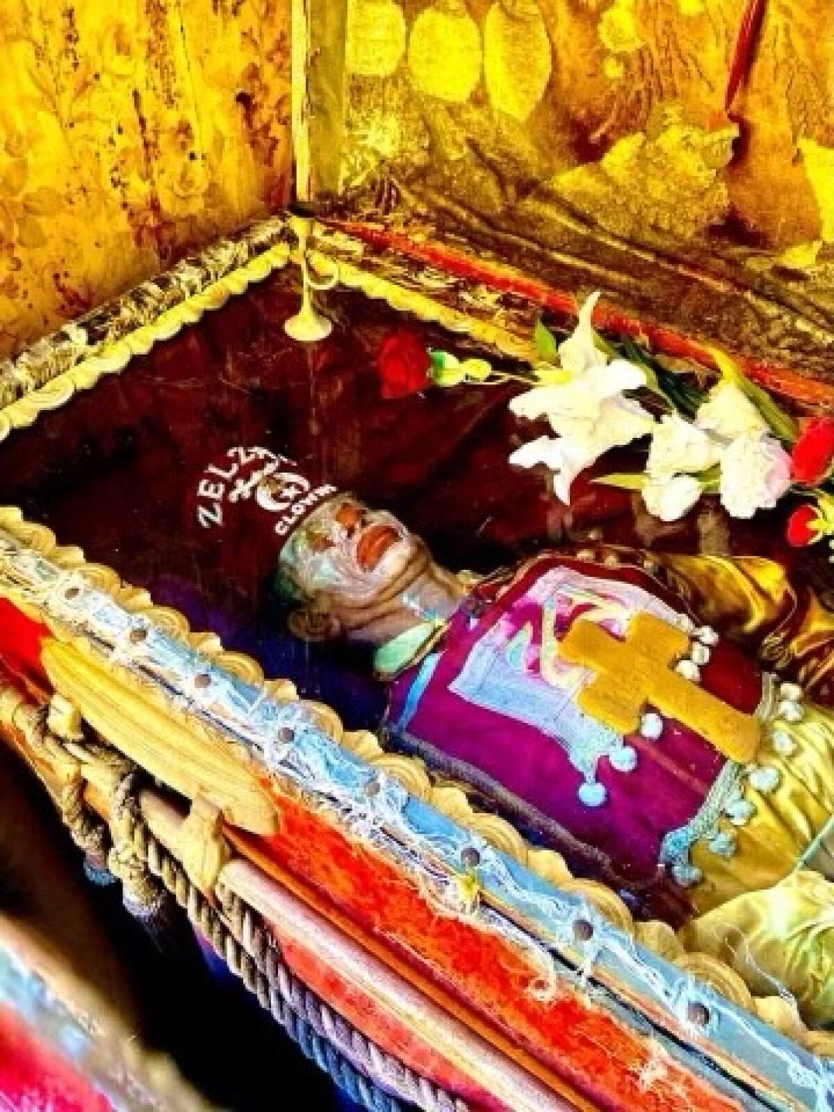 The body of a clown rests under glass in a brightly colored casket.