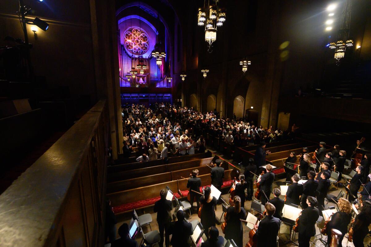 With church stained glass as the backdrop, a large crowd sits before the musicians of Civic Orchestra of Los Angeles.