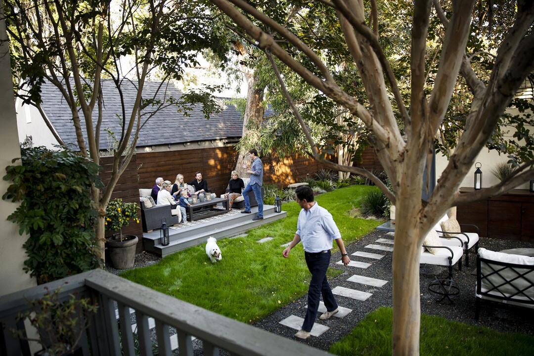 Shown is the view from Michael Moore's and Chad Rothman's deck, looking toward the three new zones of their narrow backyard: an outdoor living room set on a raised platform, left; a strip of lawn, enjoyed here by the couple's dog, Jackson; and a fire pit, bar and movie screening area at right, partially out of frame.