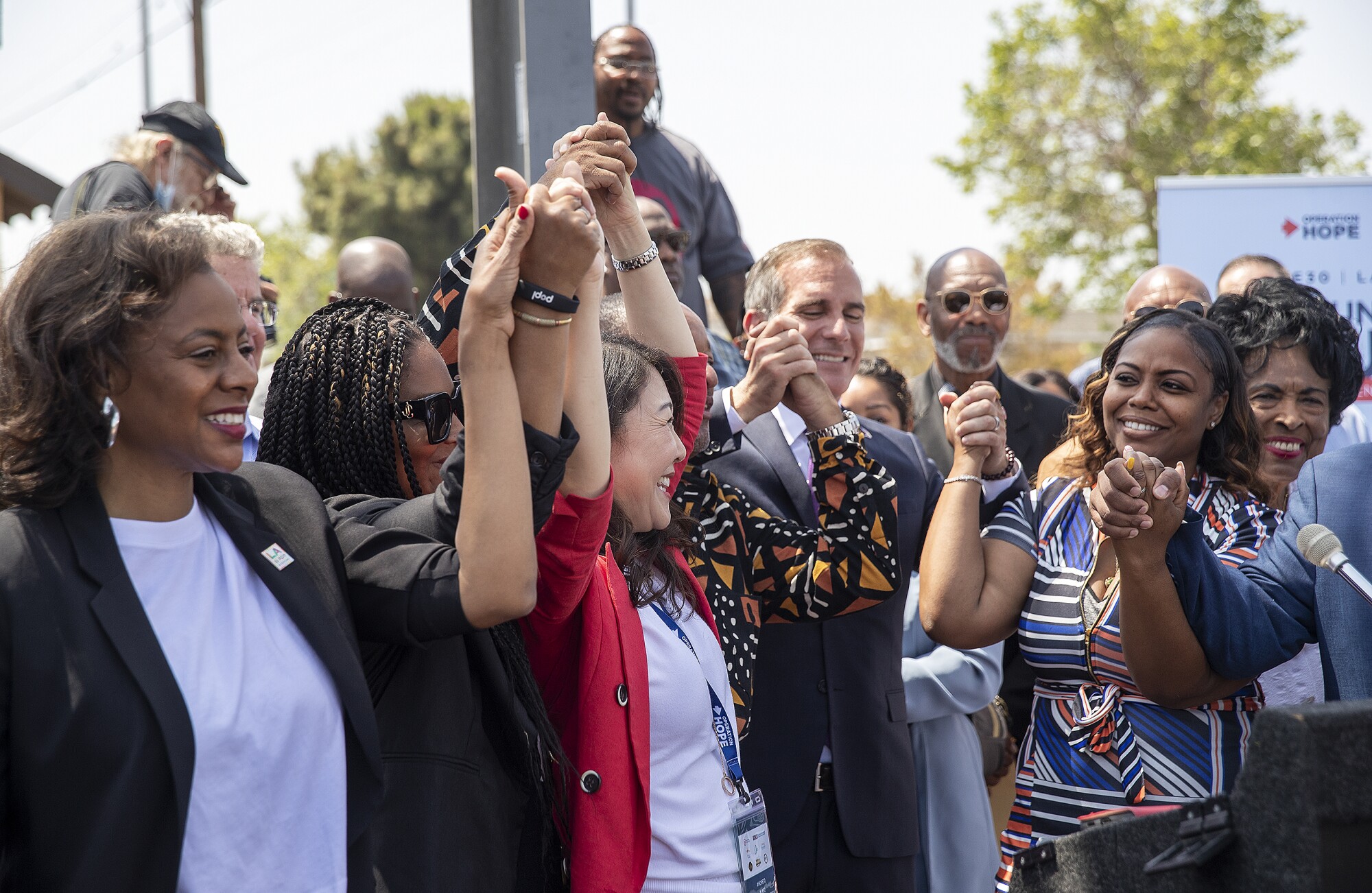 The mayor of Los Angeles raises hands with a group gathered at a news conference.