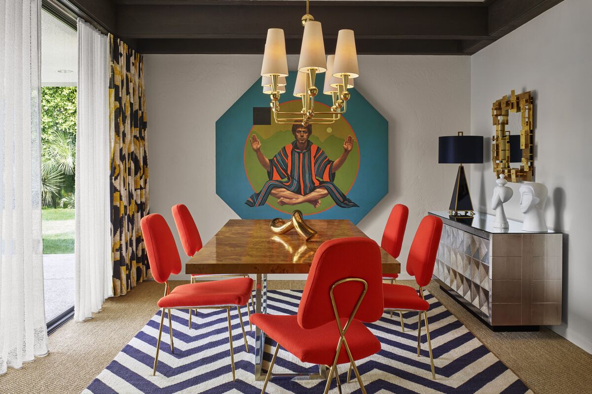 A room with a blue and white striped rug, orange chairs around a wood table and colorful art on the walls. 