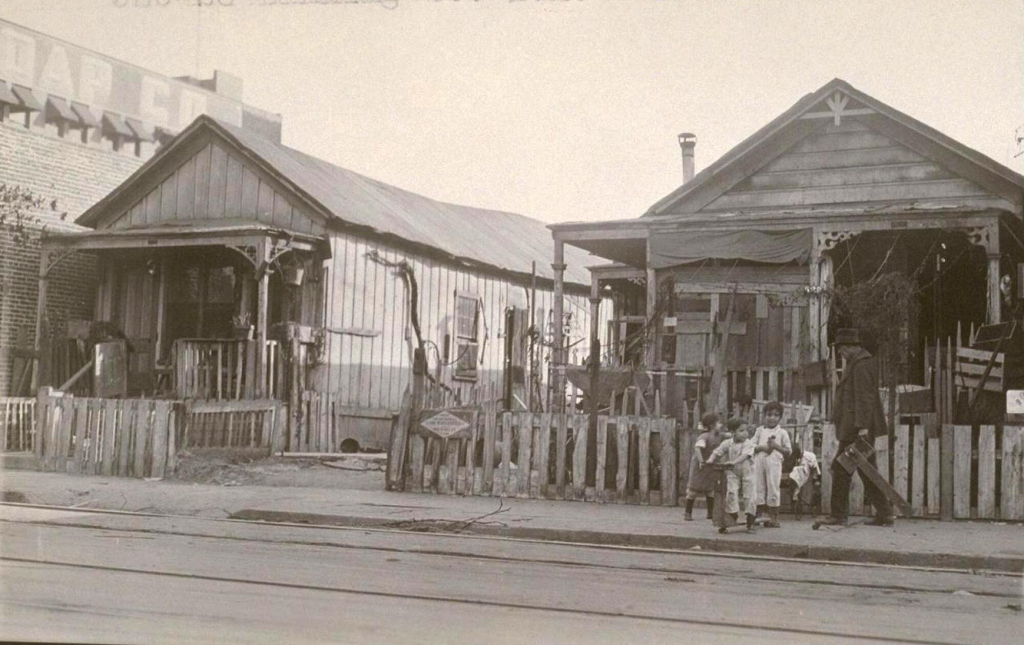 A 1924 archival image shows two wooden homes on a street with kids standing outside.