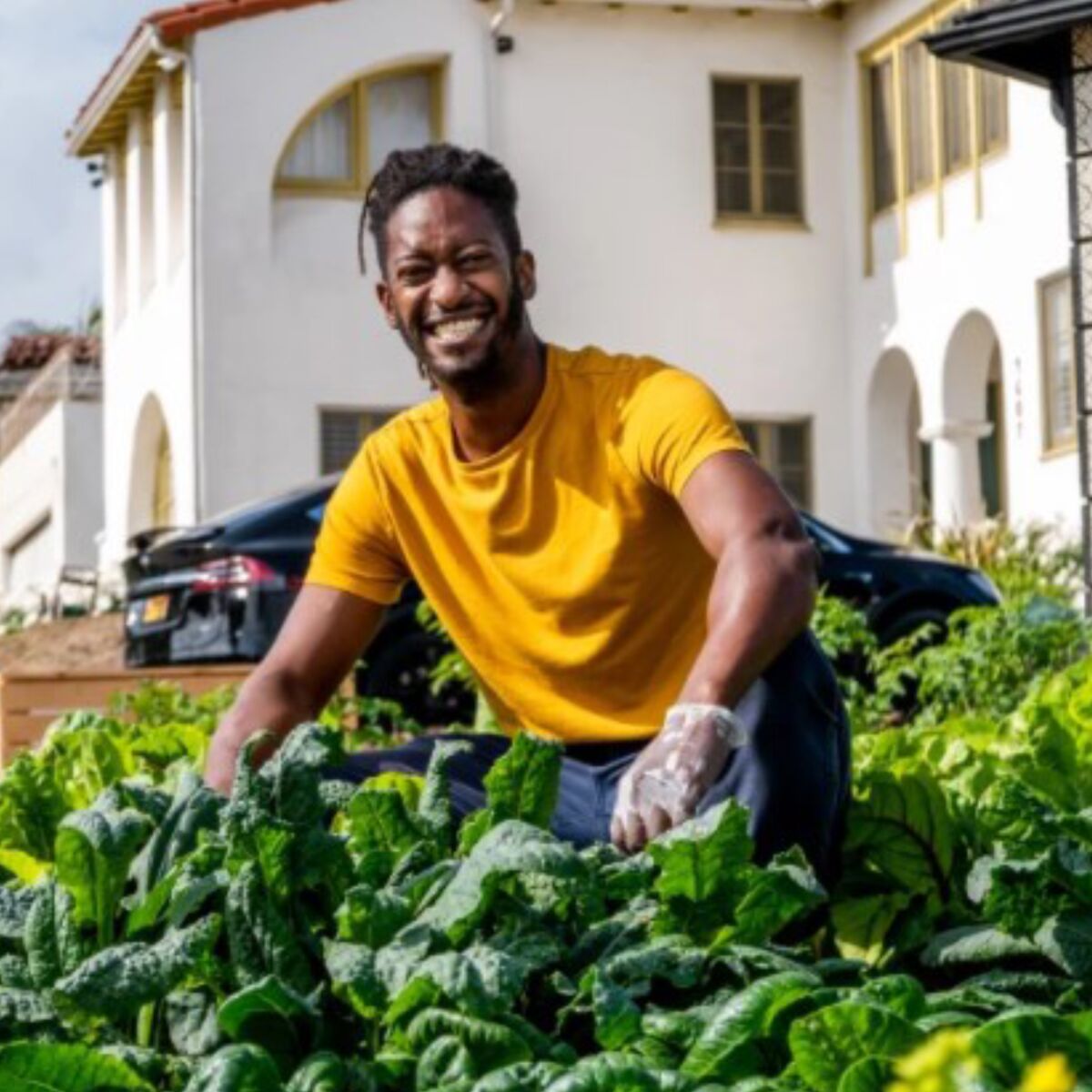 Jamiah Hargins crouches in a bed of greens in front of a house.