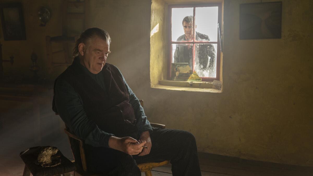 Brendan Gleeson sits in a simple room as Colin Farrell peeks in through a window in "The Banshees of Inisherin."