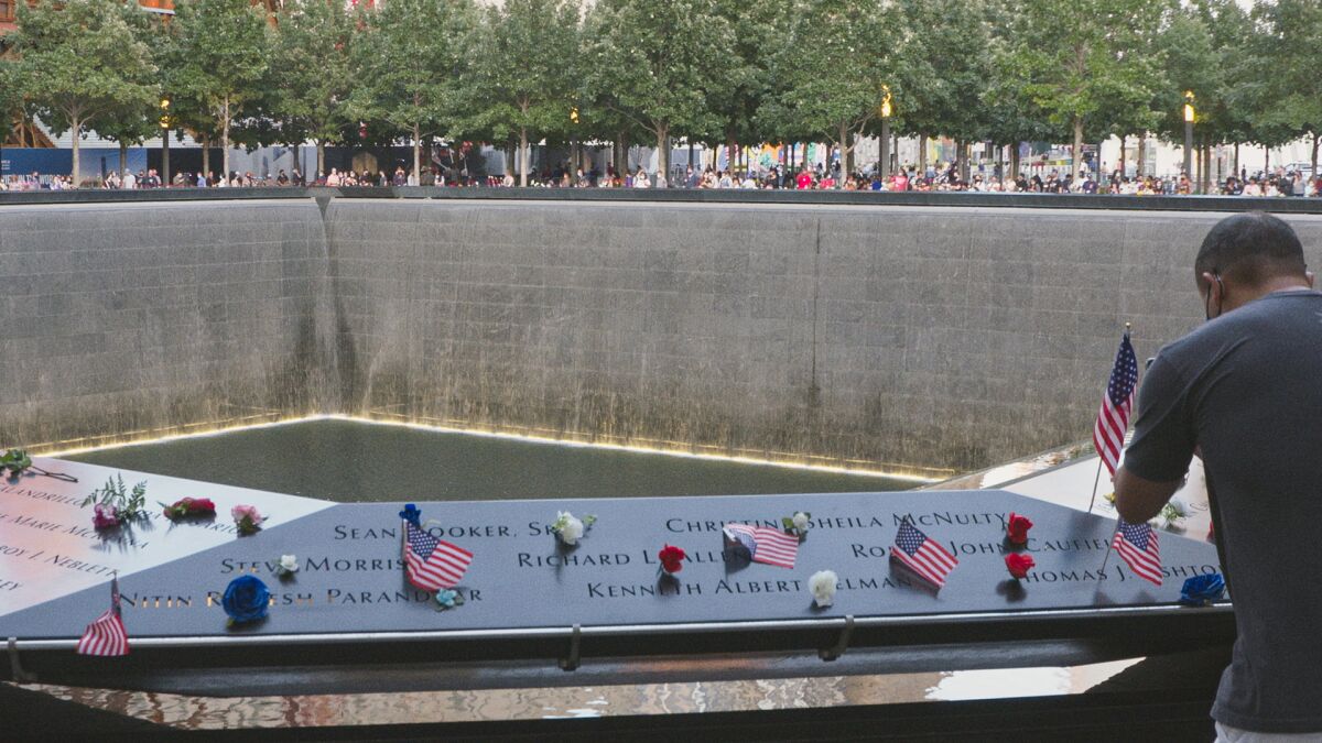 Small American flags and flowers placed on a panel of names