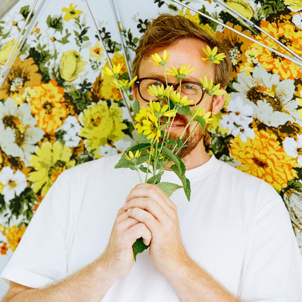 John Wilson smelling a bouquet of flowers under an umbrella.