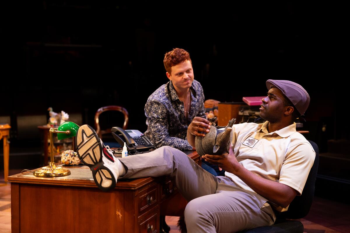 Two men in an office, a white man with red hair and a black man wearing a purple cap.