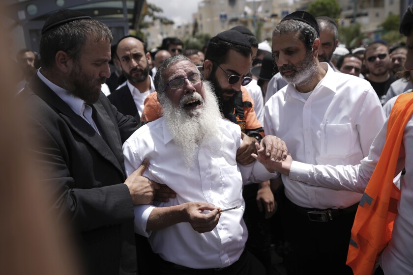 Ultra-Orthodox Jewish mourners encircle a man overcome with grief at the funeral for Yonatan Havakuk and Boaz Gol, a day after they were killed in a stabbing attack in Elad, Israel, Friday, May 6, 2022. Israeli security forces waged a massive manhunt Friday for two Palestinians suspected of carrying out the stabbing attack on Thursday near Tel Aviv that left three Israelis dead. (AP Photo/Ariel Schalit)